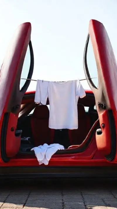 A red Ferrari with doors that open upward. A taut rope is stretched between the two doors, and freshly washed laundry is hung on this rope.