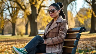 An autumn day in the park. The tall oak trees have shed their leaves, and the yellowing leaves have fallen to the ground. The sun reflects around her. A woman sits on a bench. She is in her thirties. She has white, tanned skin, black hair pulled back tightly, small oval Ray-Ban sunglasses, dark pink lipstick, and a dimpled face. She has small silver earrings. She is wearing a slim-fit light brown plaid coat, dark gray skinny jeans, and Puma green and white striped casual shoes. One arm is draped over the back of the bench. The cinematic atmosphere is alive with vibrant colors and textures. The image is filled with realistic anatomical details. The lighting is perfect for composition. Camera type: 100MP full-frame DSLR. Lens: 85mm f/1.8 portrait lens. 35mm image;